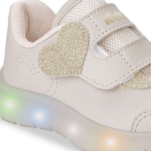 Vista lateral do tênis infantil marfim com detalhes em glitter dourado e luzes LED na sola, fechamento em velcro.